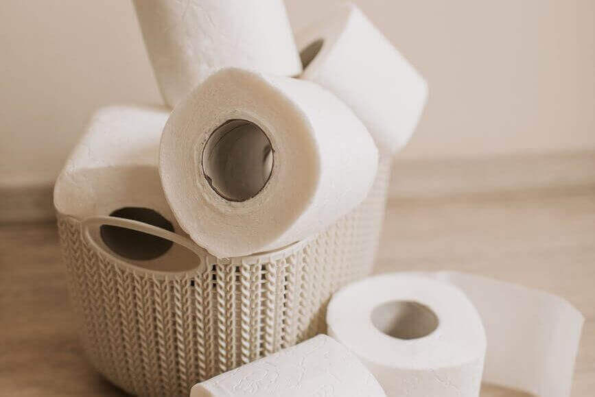 tubes of white toilet paper and plastic basket on bathroom floor